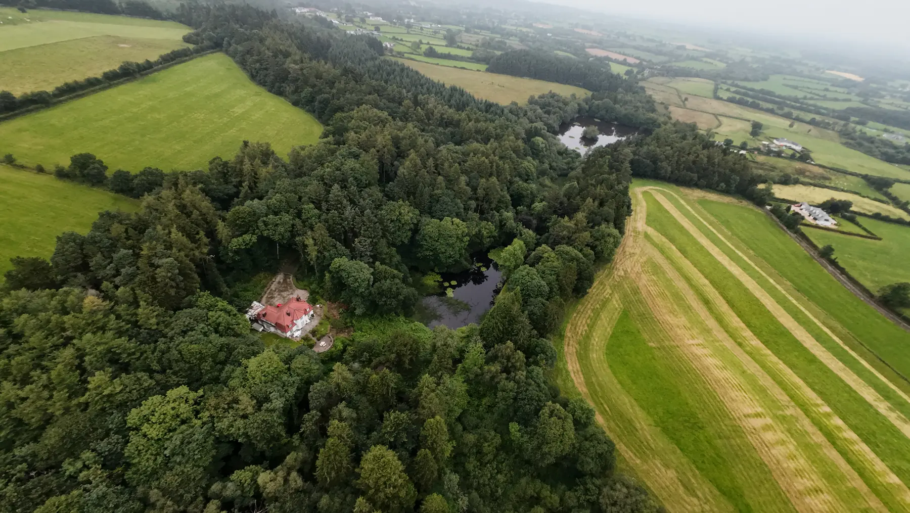 Aerial view of the woods, a lake and the red-roofed house among the trees